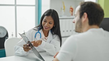 Doktor ve hasta masada oturmuş klinikteki sağlık raporlarını gösteriyorlar.