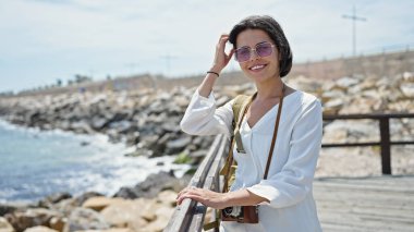 Genç ve güzel İspanyol kadın turist, deniz kenarında sırt çantası takıp gülümsüyor.