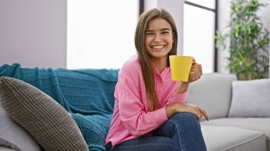 Genç ve güzel İspanyol kadın evdeki kanepede oturup kahve içiyor.