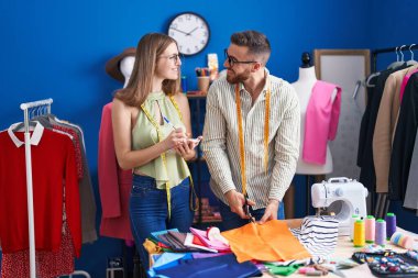 Erkek ve kadın terzi giyim fabrikasında defter üzerinde kumaş kesiyor.