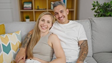 Erkek ve kadın çift evdeki kanepede oturup birbirlerine sarılıyorlar.