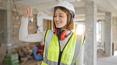 Genç sarışın mimar gülümsüyor. İnşaat alanındaki yeni evin anahtarını elinde tutuyor.