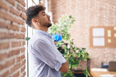 Genç Arap iş adamı ofiste kollarını kavuşturup cama yaslanıyor.
