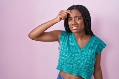 Genç Afro-Amerikan örgüleri pembe arka planda duruyor. Alnındaki sivilceden mutsuz olduğunu gösteriyor. Çirkin bir siyah nokta enfeksiyonu. sivilce ve deri problemi 