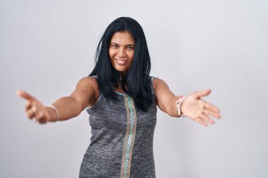 Beyaz arka planda duran olgun İspanyol kadın sarılmak için kollarını açmış kameraya bakıyor. Mutluluğu kucaklayan neşeli bir ifade.. 