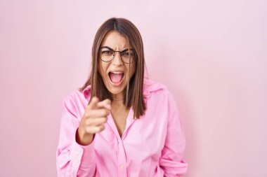 Pembe arka planda duran gözlüklü genç İspanyol kadın kameraya kızgın ve sinirli olduğunu gösteriyor. 