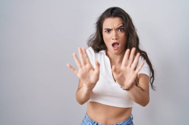 Genç bir kız beyaz arka planda duruyor. Avuçlarını hareket ettiriyor. Korkmuş ve iğrenç bir ifadeyle reddediyor. Dur ve yasakla. 