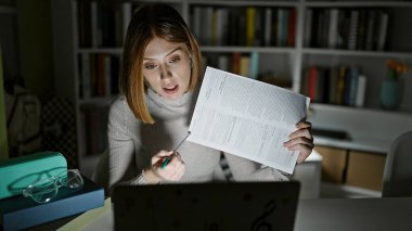 Kütüphanede evrakları gösteren bir video görüşmesi yapan sarışın genç bir kız öğrenci.