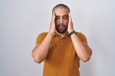 Beyaz arka planda duran sakallı İspanyol bir adam, eli başının üstünde, stres yüzünden başı ağrıyor. migren ağrısı. 