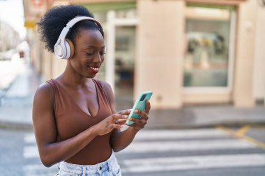 Afro-Amerikalı kadın gülerek sokakta müzik dinliyor.
