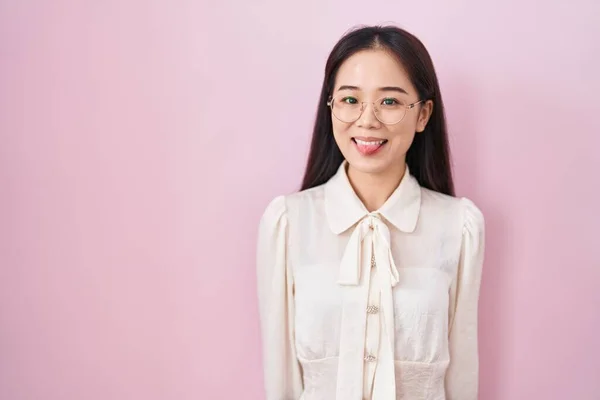 年轻的中国女人站在粉色的背景上 用滑稽的表情把舌头伸出来 高兴极了 情感概念 — 图库照片