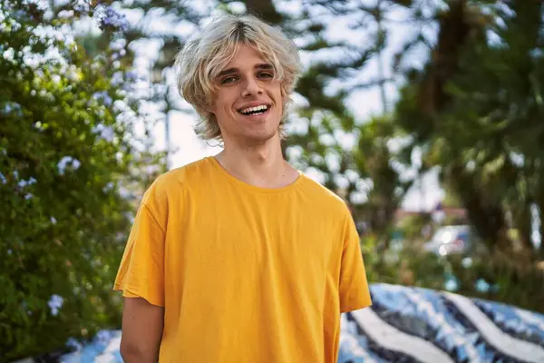 Young blond man smiling confident standing at park