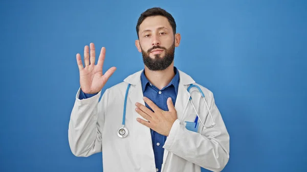 年轻的惊慌失措的男医生 手托着胸膛在孤零零的蓝色背景下宣誓 — 图库照片