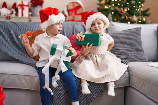 Δύο Παιδιά Κρατώντας Δώρα Κάθεται Στον Καναπέ Από Χριστουγεννιάτικο Δέντρο — Φωτογραφία Αρχείου