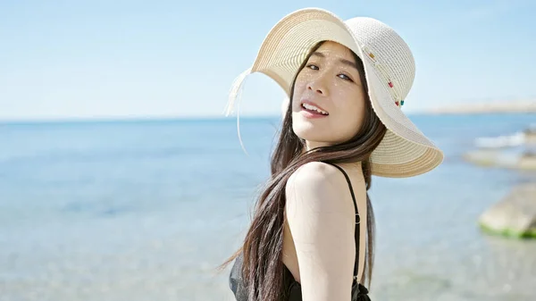 Young chinese woman tourist smiling confident wearing swimsuit and summer hat at seaside