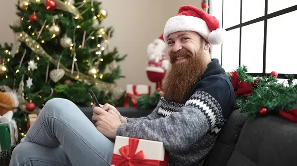 Νεαρός Κοκκινομάλλης Που Χρησιμοποιεί Smartphone Κάθεται Στον Καναπέ Από Χριστουγεννιάτικο — Φωτογραφία Αρχείου