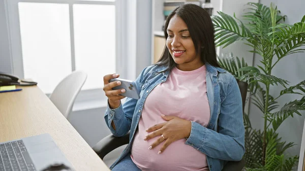 年轻的怀孕女工在办公室观看智能手机触摸腹部的视频 — 图库照片