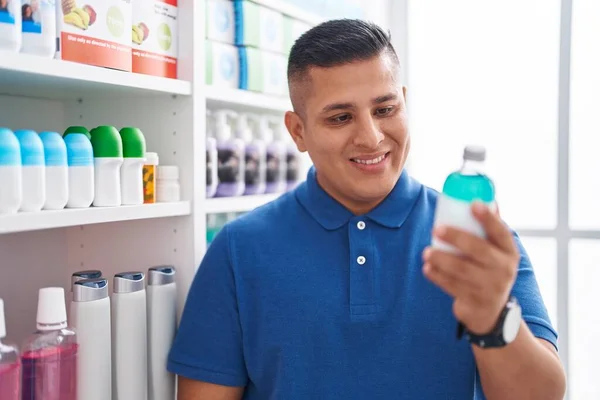 Young latin man customer smiling confident holding medication bottle at pharmacy