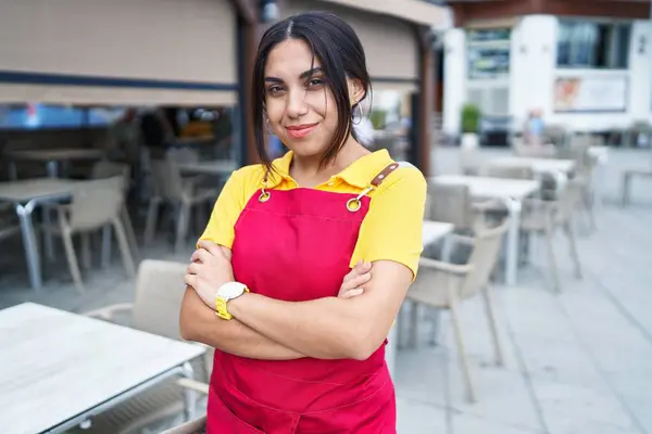 Young beautiful arab woman waitress smiling confident standing with arms crossed gesture at coffee shop terrace