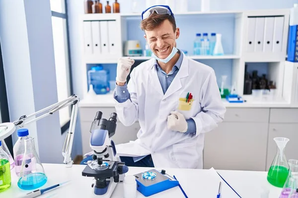 Bilim adamlarının laboratuarında çalışan beyaz adam, kolları havada ve gözleri kapalı bir şekilde başarının şaşkınlığını ve şaşkınlığını yaşıyor. 