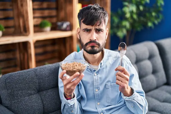 Young hispanic man with beard eating healthy whole grain cereals depressed and worry for distress, crying angry and afraid. sad expression.