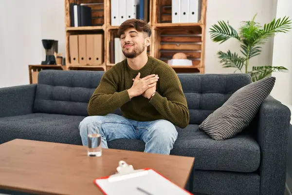 Arab man with beard working on depression at therapy office smiling with hands on chest, eyes closed with grateful gesture on face. health concept.