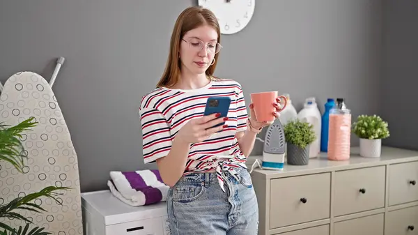 Genç Sarışın Kadın Akıllı Telefon Kullanıyor Kahve Içiyor Çamaşır Odasında — Stok fotoğraf