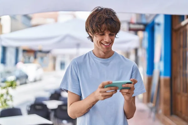 Young blond man smiling confident watching on smartphone at street