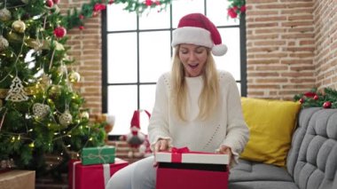 Genç mutlu sarışın kadın oturma odasında Noel hediyesini açıyor.