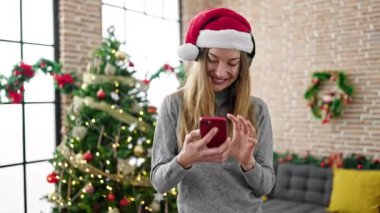 Noel Baba şapkalı ve kulaklıklı mutlu genç kadın cep telefonu kullanıyor.