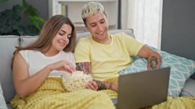 Dizüstü bilgisayarda film izleyen güzel bir çift evde patlamış mısır yiyor.