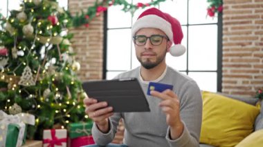 Noel Baba şapkası takan, tabletli bir adam ve bir fincan çay.