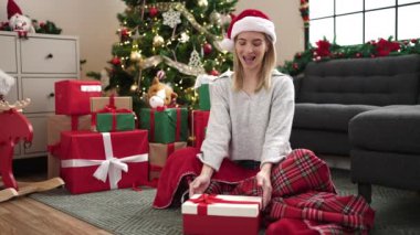 Noel Baba şapkalı mutlu genç kız oturma odasında Noel hediyeleriyle oturuyor. 