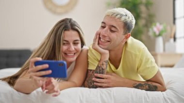 Güzel bir çift yatak odasında uzanmış akıllı telefondan video izliyor.
