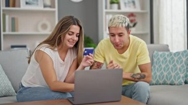 Laptop ve kredi kartıyla alışveriş yapan güzel bir çift evdeki koltukta oturuyor.