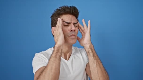 孤立した青い背景で頭痛に苦しむ若いヒスパニック男性 — ストック動画