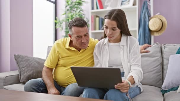 西班牙裔父亲和女儿自信地使用笔记本电脑 坐在舒适的客厅沙发上庆祝胜利 他们的笑容闪烁着爱和幸福的光芒 — 图库视频影像