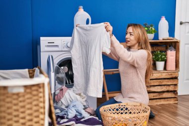 Çamaşırhanede çamaşır yıkayan tişörtlü genç bir kadın.