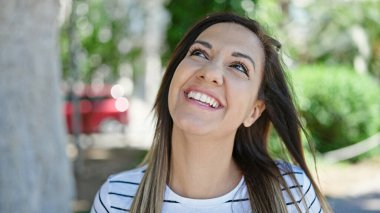 Orta Doğulu bir kadın gülümsüyor. Parka bakıyor.