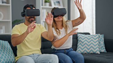 Kadın ve erkek evde sanal gerçeklik gözlüğü kullanarak video oyunu oynuyorlar.