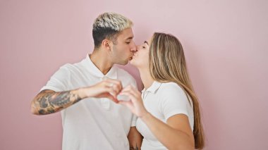 Güzel bir çift bir arada durmuş pembe arka planda öpüşürken kalp hareketi yapıyor.