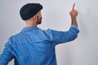 Sakallı İspanyol bir adam arka planda dikiliyor. Parmak eliyle öne doğru poz veriyor. 