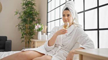 Bornoz giymiş genç ve güzel bir İspanyol kadın yatak odasında şampanya içiyor.