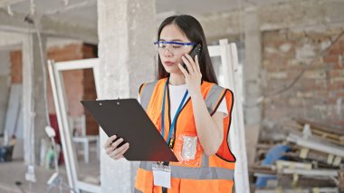 İnşaat raporlarını okuyan Çinli genç müteahhit inşaat alanında akıllı telefondan konuşuyor.