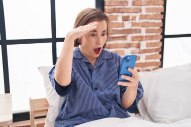 Orta yaşlı bir kadın yatak odasında akıllı telefon kullanıyor.