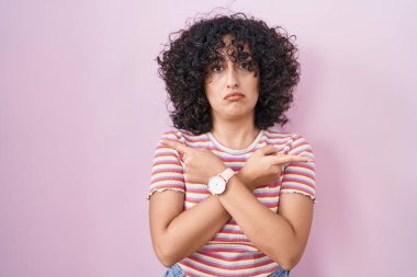 Pembe arka planda duran genç ortadoğulu kadın her iki tarafı da parmaklarıyla işaret ediyor. Farklı yönler farklı. 