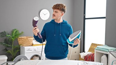 Genç İspanyol adam çamaşır odasında ütü makinesini seçiyor.