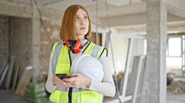 İnşaat alanında akıllı telefon kullanan genç sarışın bir mimar.