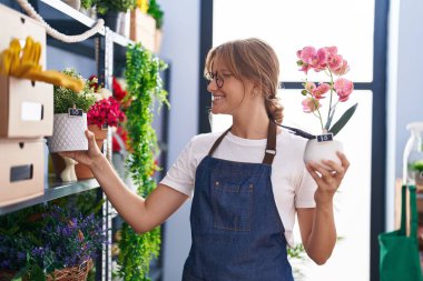 Çiçekçiye saksı tutarken gülümseyen sarışın kız.