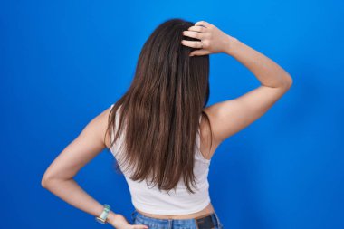 Young caucasian woman standing over blue background backwards thinking about doubt with hand on head 